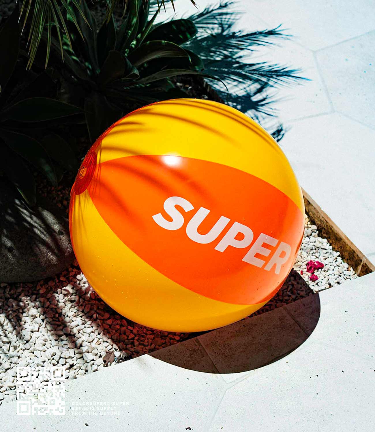 Bright orange and yellow inflatable beach ball with "Super" text, perfect for seaside fun, placed on a sunny poolside.