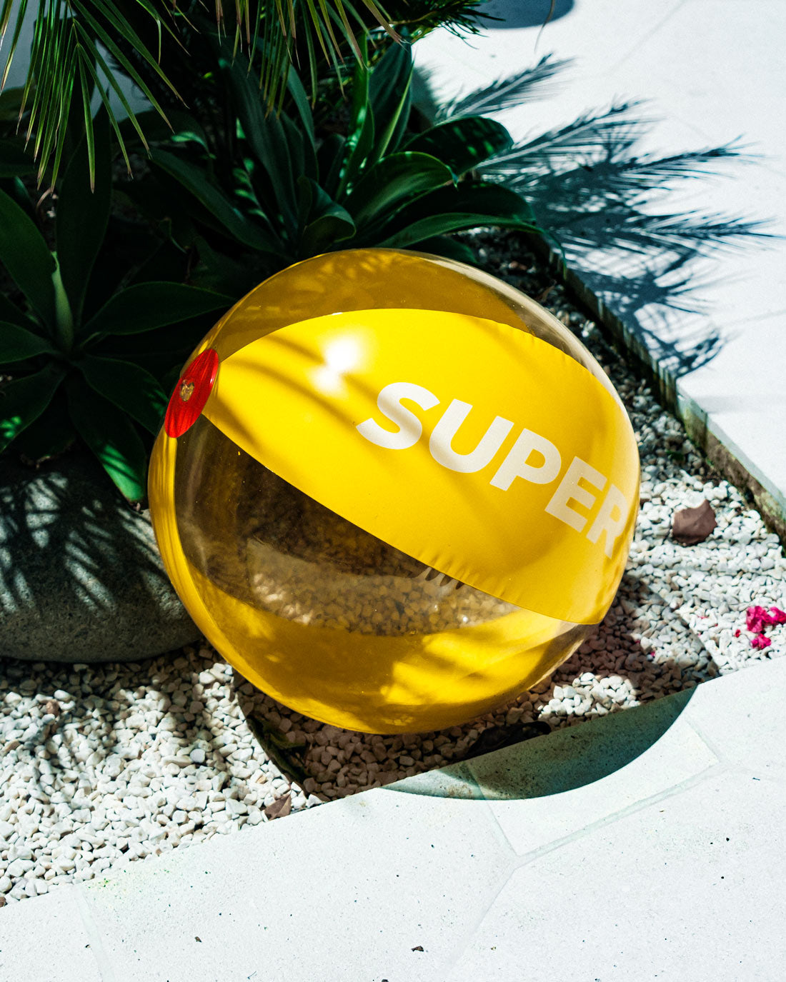 Bright orange and yellow inflatable beach ball with "Super" text, perfect for seaside fun, placed on a sunny poolside.