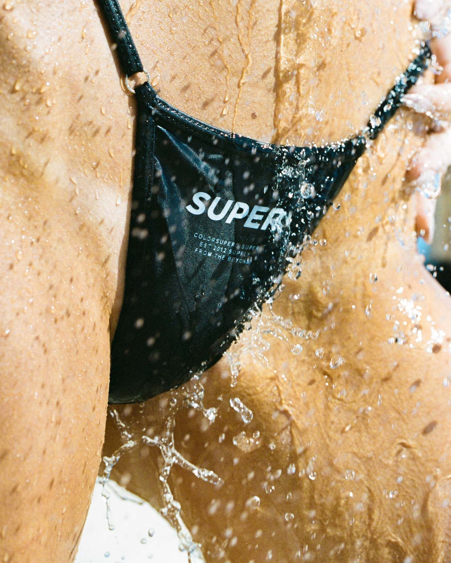 Black thong bikini with water splashes, showcasing high-quality fabric and a distinctive design perfect for beachwear.
