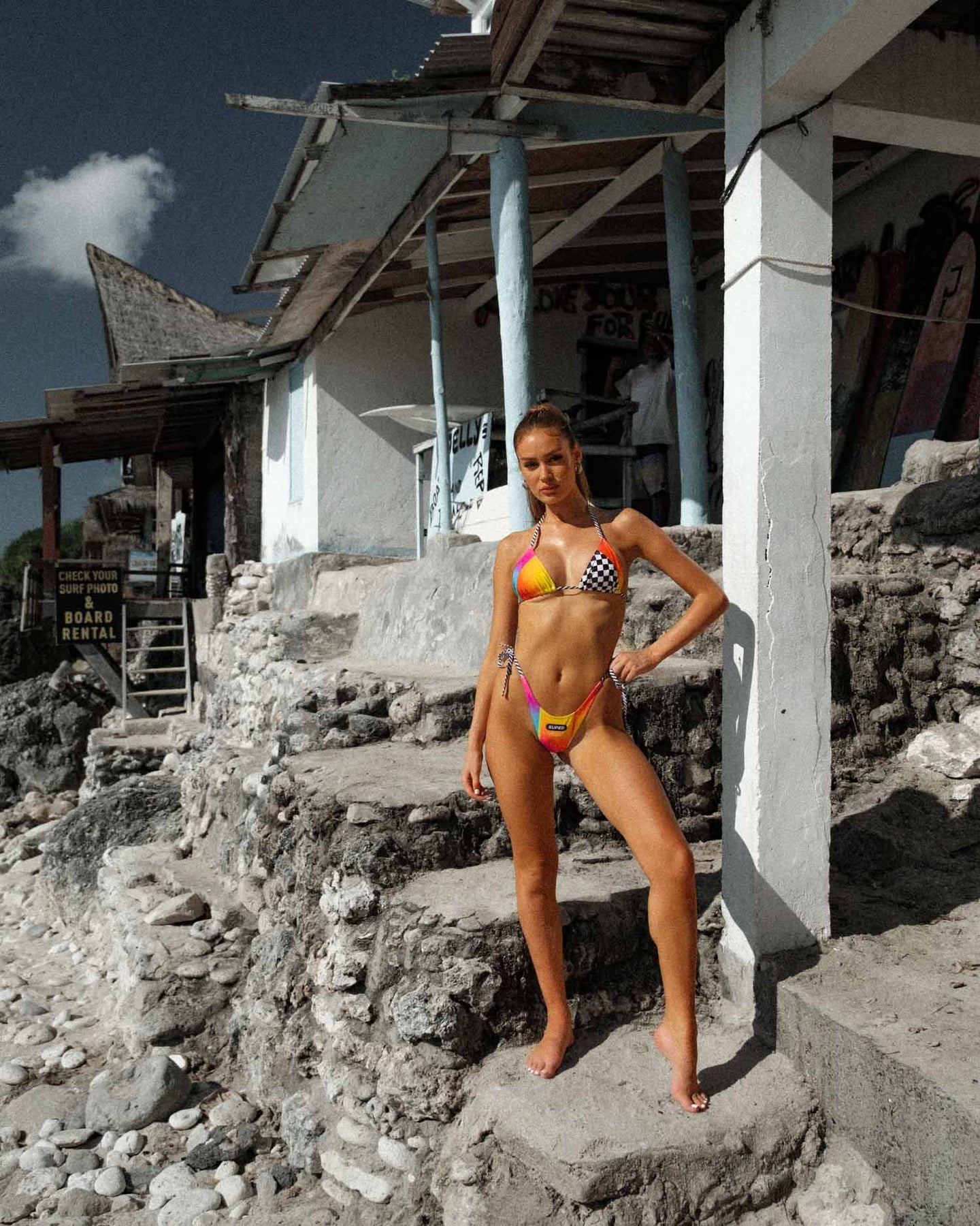 Front full-body shot of the model posing in the Triangle Design Low Rise Visual Formula Brazilian Bikini with tie sides and ombre print by the beach.