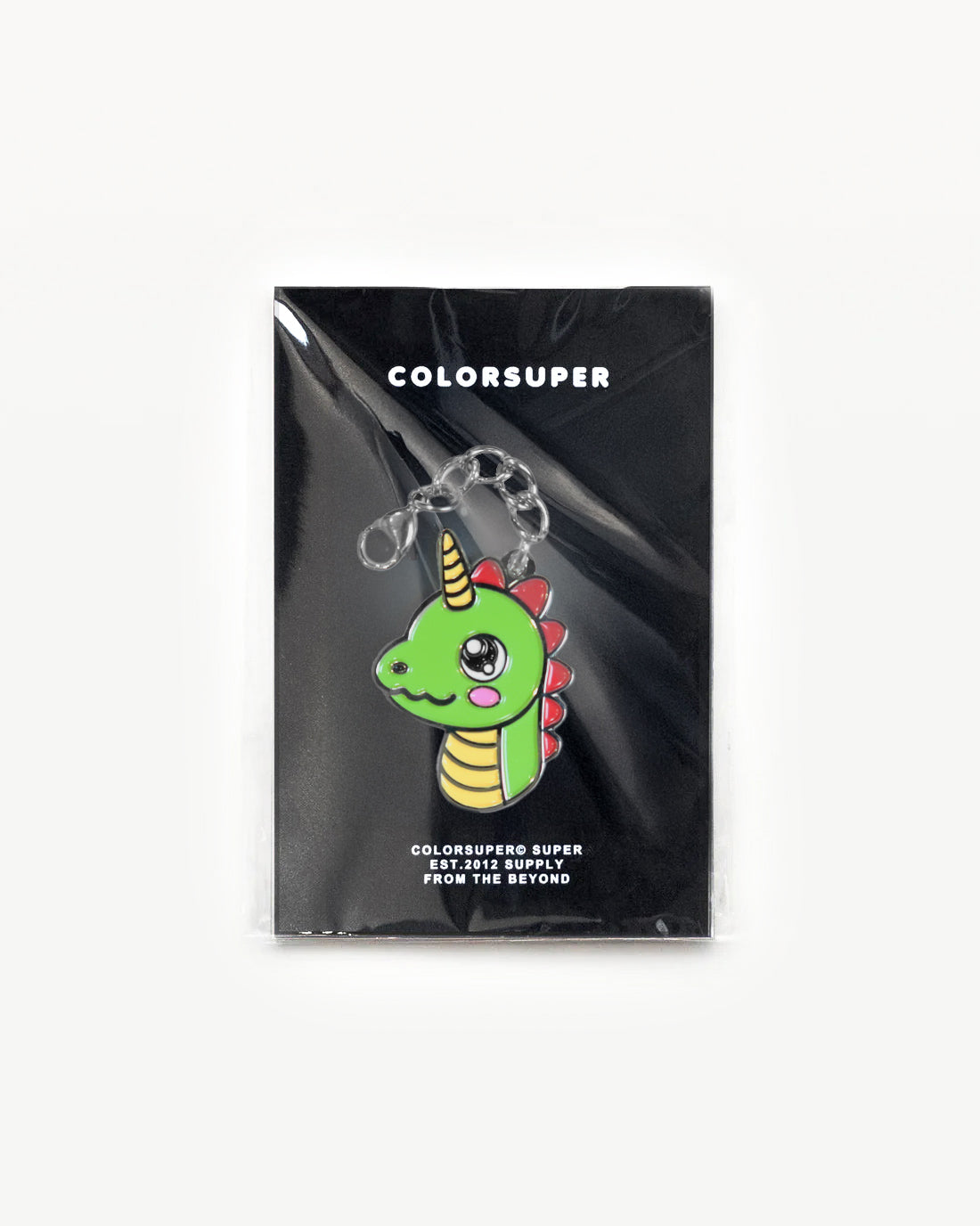 Bright green Cute Dino charm with a gold horn on a black packaging background.