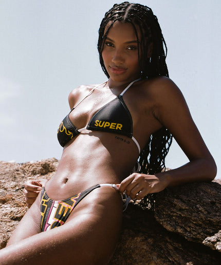 A model radiates style in a black bikini featuring the classic SUPER logo. The high-waisted thong design, along with adjustable sides, adds a touch of sophistication to this chic summer bikini statement.