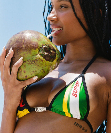 Close-up shot of the model enjoying a coconut drink, highlighting the top details and charm bar of the High Waisted Triangle design High Shot Rio Brazilian Bikini with adjustable sides and graphic prints.