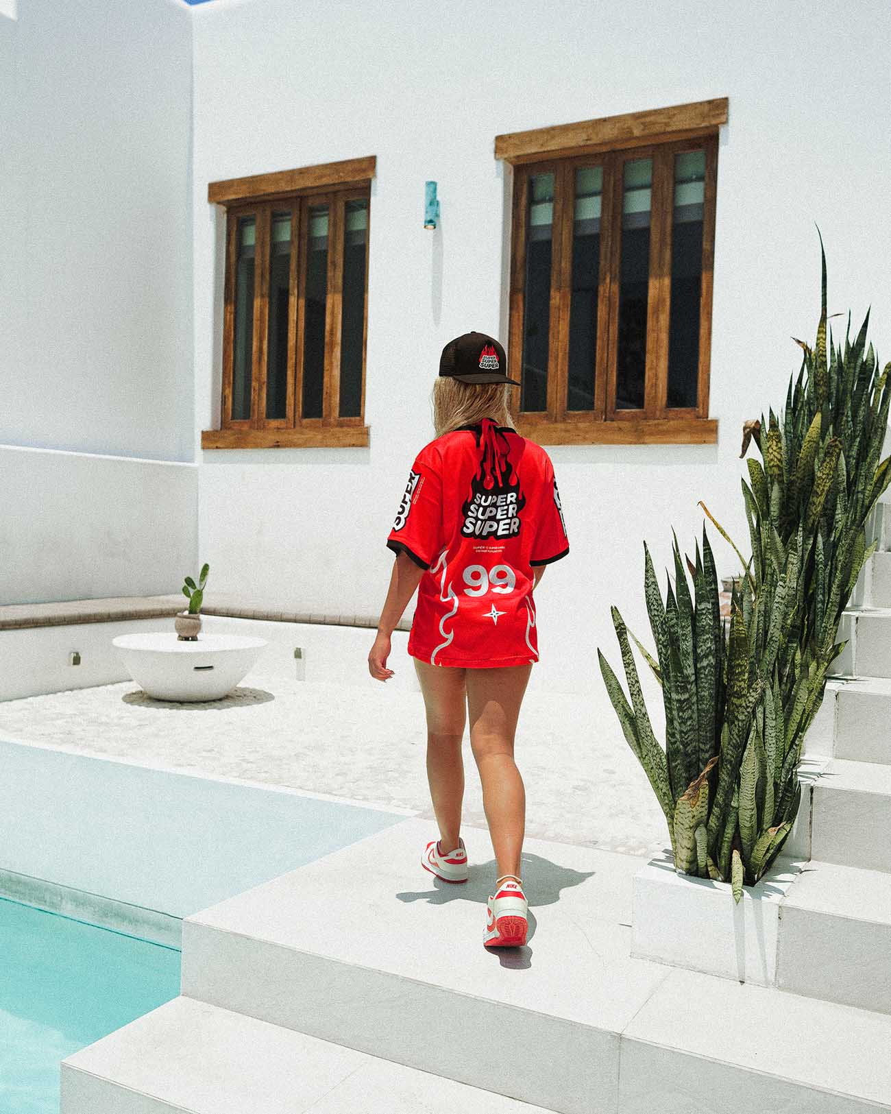 Model wearing an oversized red mesh jersey by Heat, walking in a sunlit outdoor setting, perfect for summer activities.