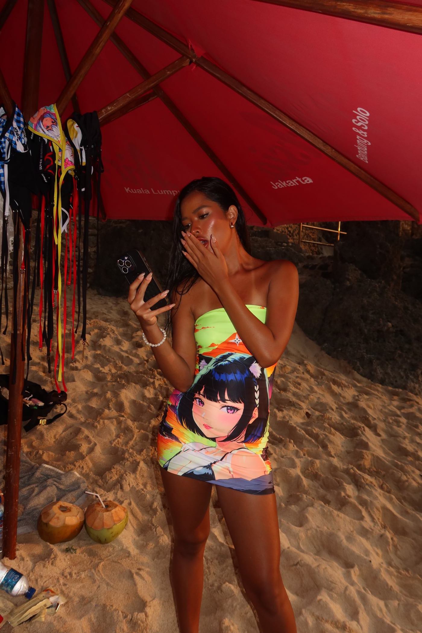 Woman wearing Volcanic Tube Dress with fierce anime girl design at a beach under a red umbrella.